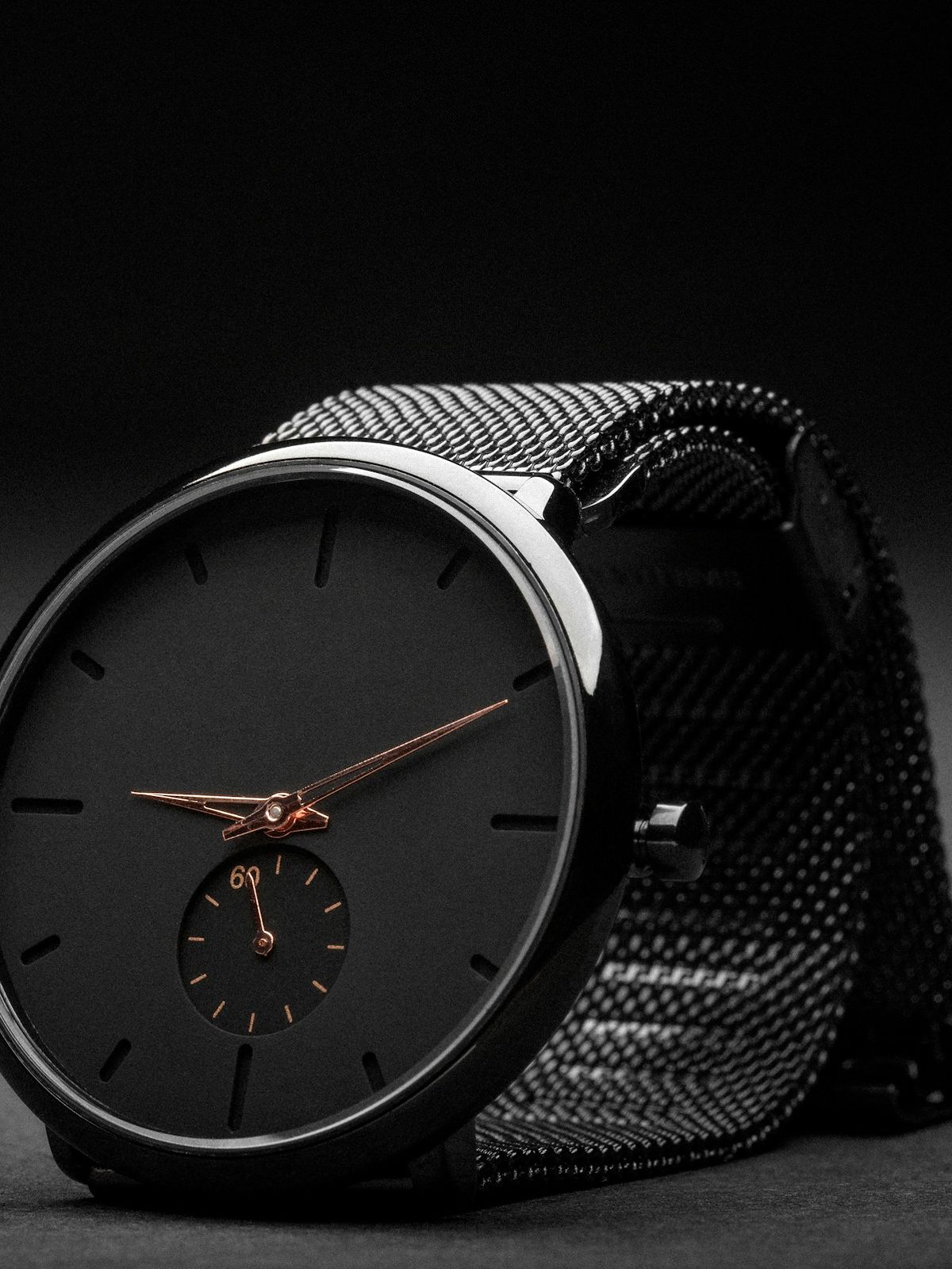Schlichte schwarze Armbanduhr mit roségoldenen Zeigern und Milanaise-Armband im Streiflicht