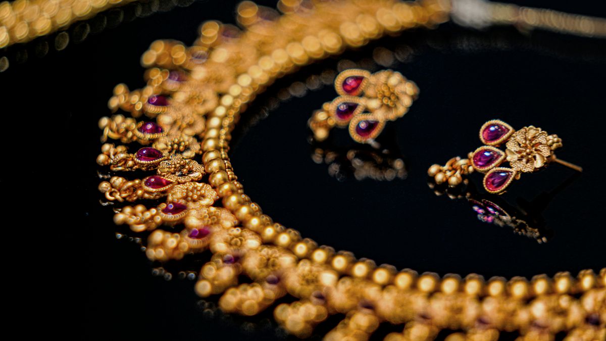 Goldenes Collier mit roten Steinen und passende Ohrringe auf spiegelndem schwarzem Grund